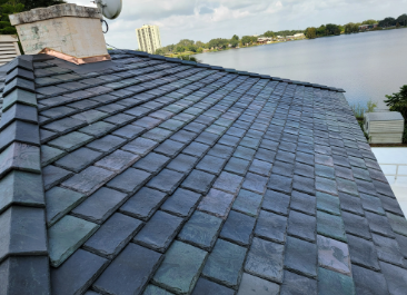 A_close_up_of_a_slate_roof_with_a_river_and_trees_in_the_background.