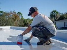 A_person_applying_coating_on_a_white_rooftop_with_a_paint_can_and_brush.

