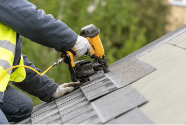 Worker_in_safety_gear_using_nail_gun_on_roof_shingles.